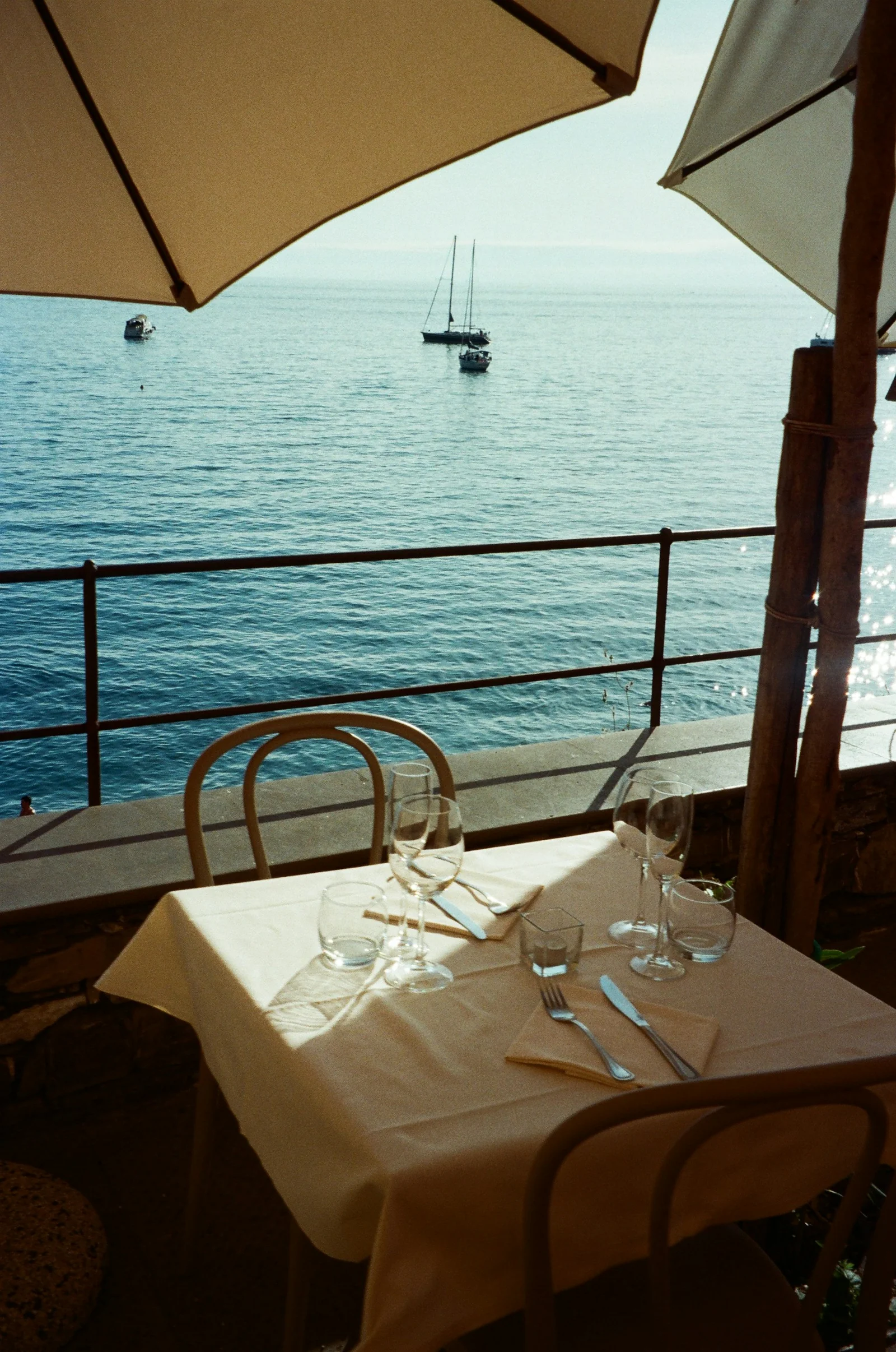Table dressée avec une nappe claire sous un parasol, face à la mer. Lieu non précisé par la photographe.